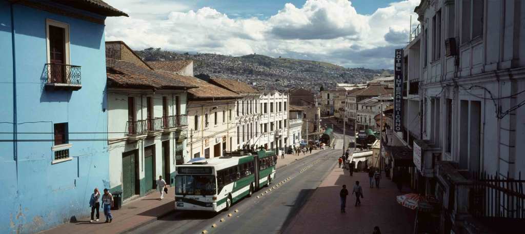 A white and green bus drives down a street in Quito, Ecuador.