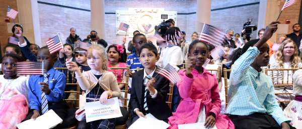Children wave American flags after taking the Oath of Allegiance as they become U.S. citizens. Credit: Anthony Behar/Sipa USA
