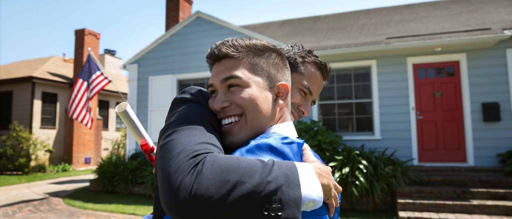Hispanic father is congratulating his son in front of their home on graduation day.