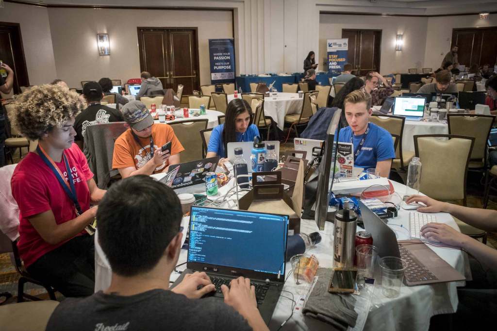 Group of young people sitting at a round table on their computers participating in a hackathon.