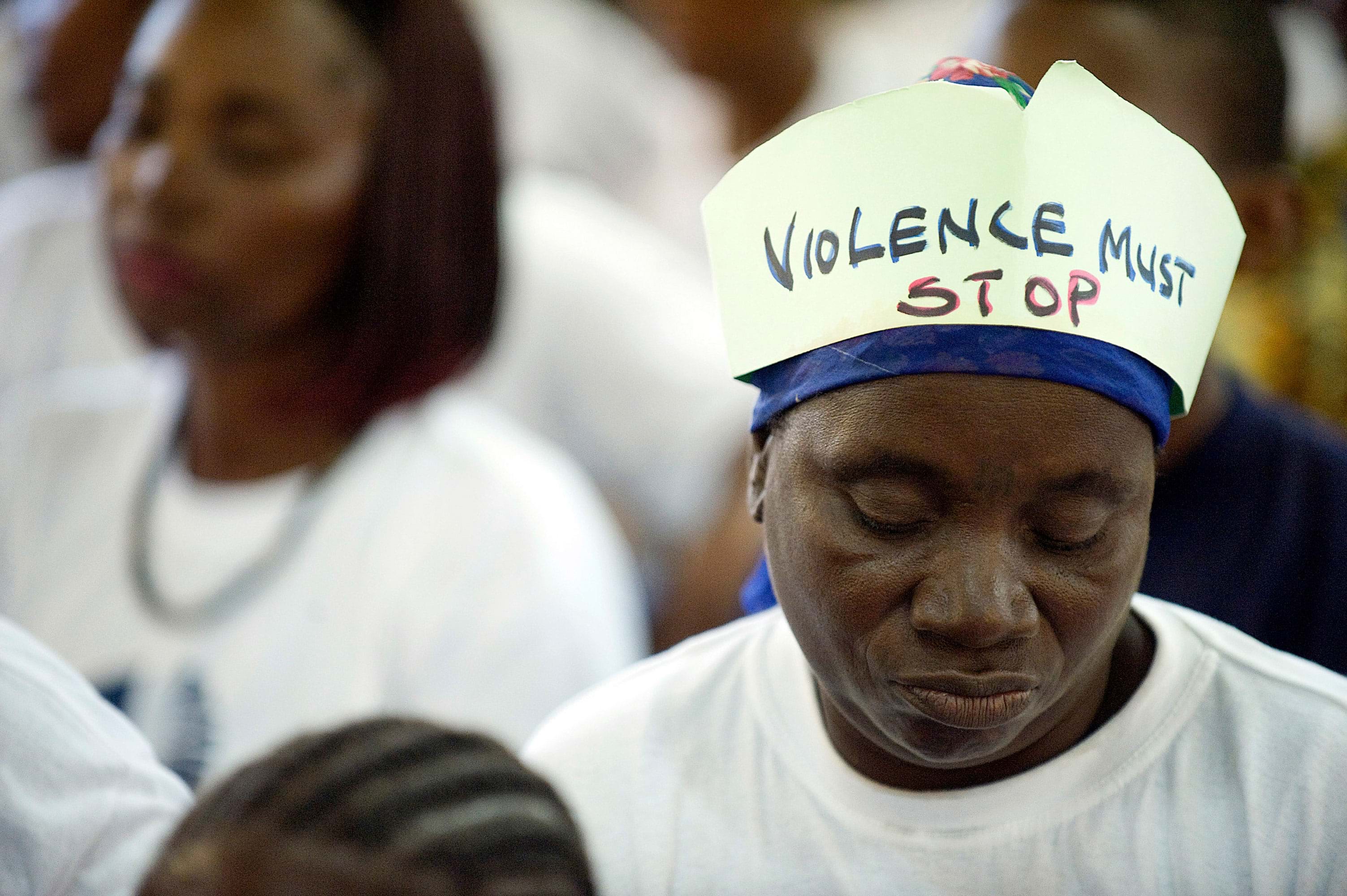 A Black person wears a hat with "Violence Must Stop" handwritten on it.