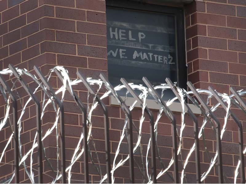 A handmade sign that reads “Help, we matter 2” hang in a cell window of a prison guarded by barbed wire.