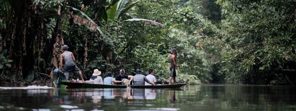 A man powers a canoe with a delegation from Ford indigenous grantee AMAN while a local guide stands at the front and looks ahead in a dense forest. Photo by Kynan Tegar