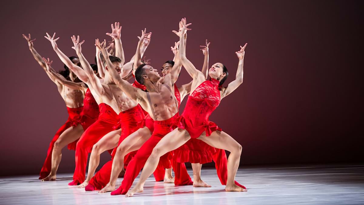 Group of dancers wearing red with their arms raised in the air.