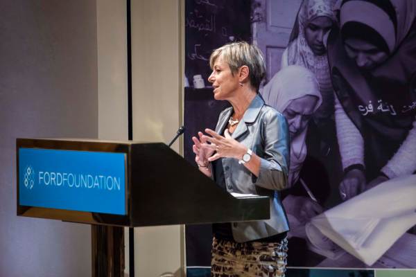Hilary Pennington is wearing a shiny grey jacket, gesturing with her hands as she speaks at a Ford Foundation gathering.