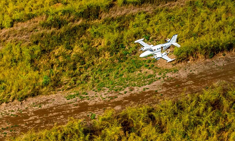 A white plane comes down for a landing on a secret dirt landing strip in the Guatemalan forest.