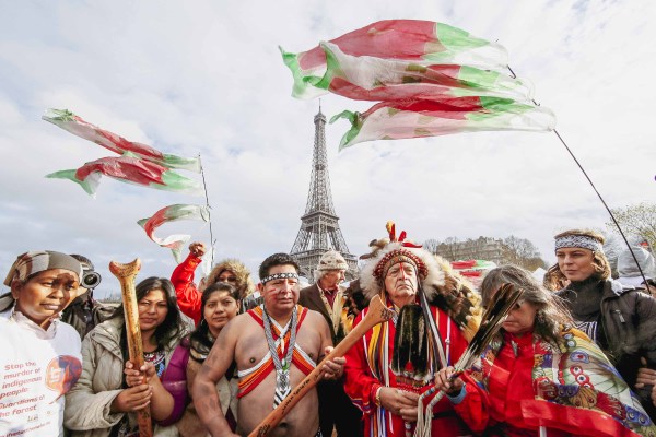  Indigenous Peoples from around the world wearing traditional clothes on a ferry on the Paris Seine River, behind them is the Eiffel Tower. With their canoe destroyed during COP21 in Paris, the alliance boarded a ferry on the Seine and invited Indigenous leaders from the North Pacific and the media to join their #PaddletoParis action. This ferry ride became the iconic image published on news outlets worldwide when Indigenous rights were recognized in the Paris Climate Change Agreement.
