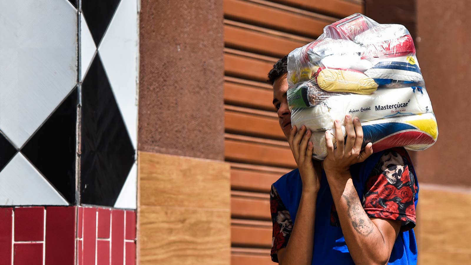 A Brazilian man carries a heavy plastic-wrapped package of food on his shoulder.
