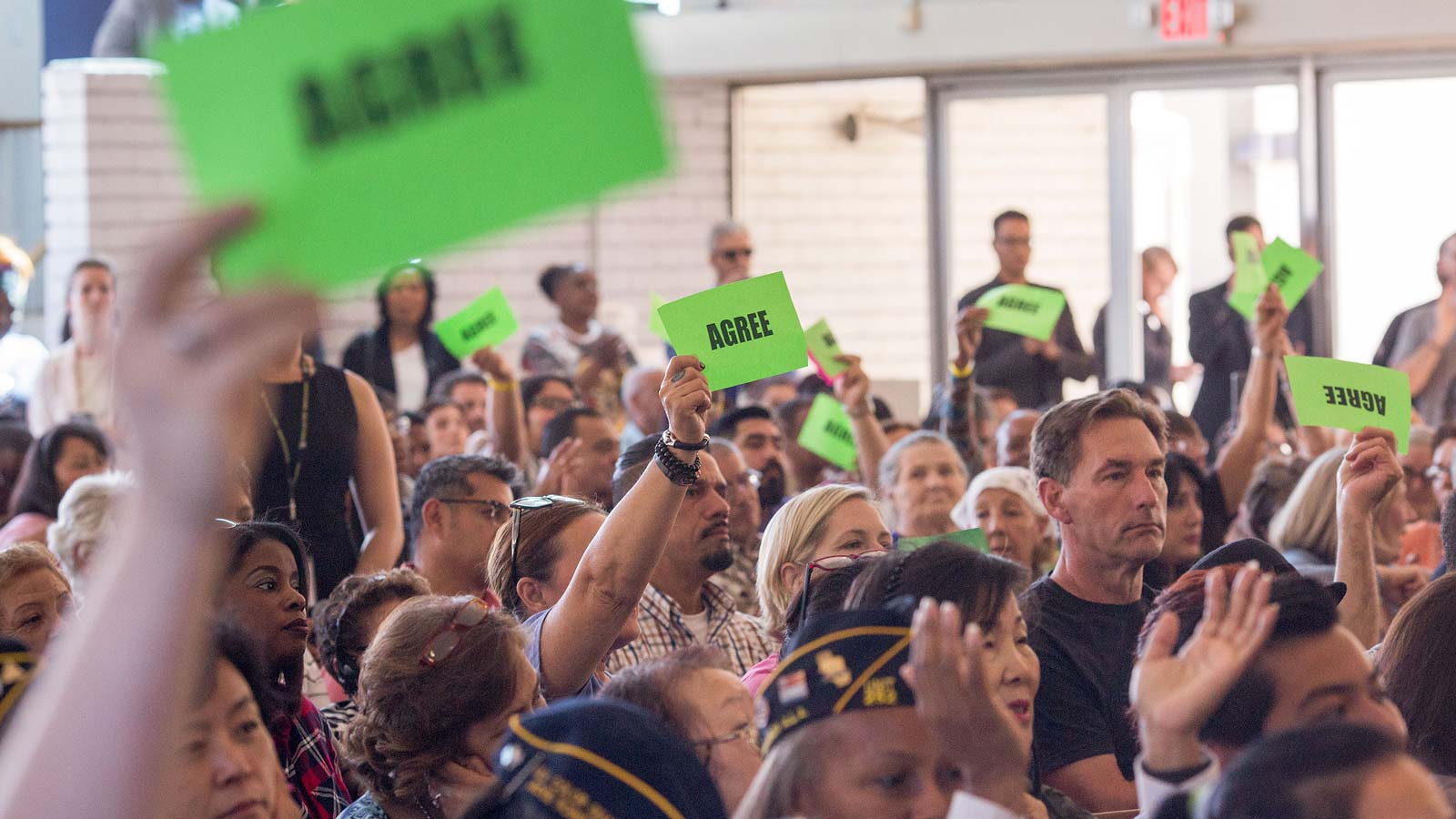A crowd at a town hall holding up green sights that read “Agree.”