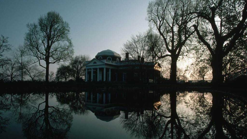 A dimly lit photo of Thomas Jefferson’s Monticello reflected in a small water pool.