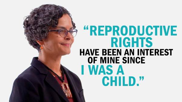 Lourdes Rivera has short dark curly hair and is wearing dark-rimmed glasses, earrings with an orange stone, a black blazer and burgundy top, and a large pendant necklace. Next to her is copy that reads, "Reproductive rights have been an interest of mine since I was a child."