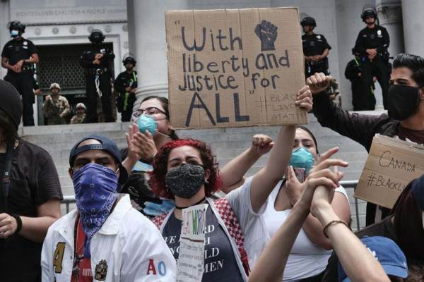 Protestors wore face masks and held signs, one of which reads "with liberty and justice for all." While police guarded the entrance to the building, they were protesting in front.