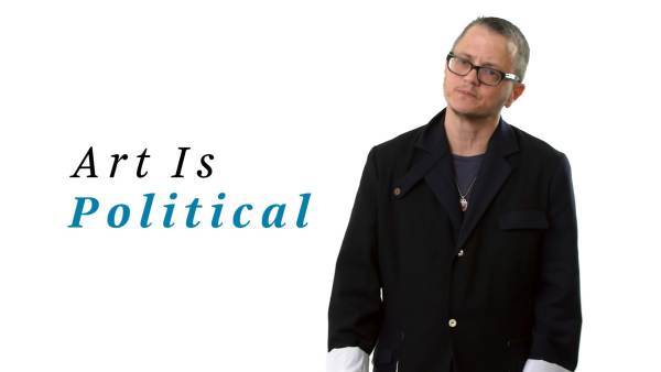 P Carl wears a black blazer with white rolled-up sleeves over a dark gray crew neck t-shirt. The phrase "Art Is political" appears to the left.
