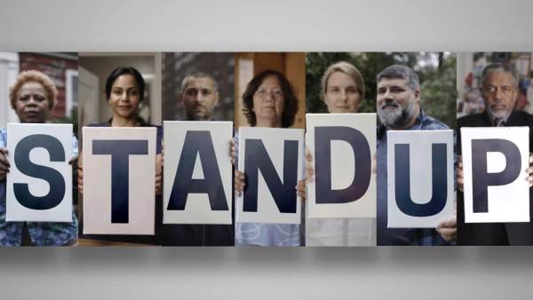 Image of individuals holding letter signs spelling "Stand up."