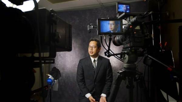 Jeff Chang sitting on a film set in front of multiple cameras with his face displayed on all monitors. 