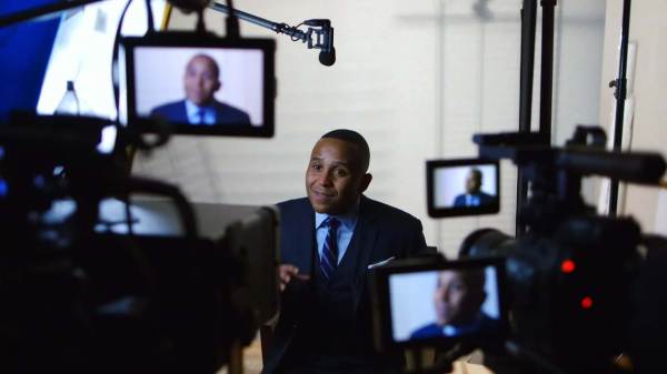 Rashad Robinson sitting on a film set in front of multiple cameras with his face displayed on all monitors. 