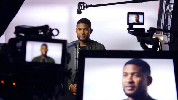 Usher sitting on a film set in front of multiple cameras with his face displayed on all monitors. 