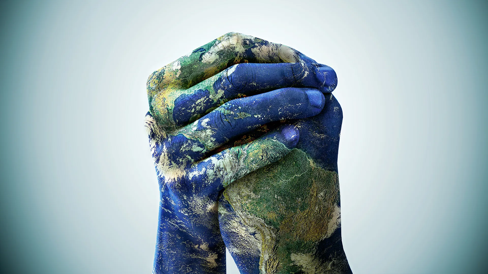 Two hands clasped together, painted to resemble the Earth's surface with details including blue oceans and green-brown land masses, symbolizing unity and global cooperation, set against a light blue background.